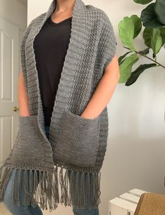 a woman standing in front of a door wearing a gray knitted shawl with fringes