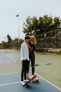 two people standing on top of a tennis court with their arms around each other as they kiss