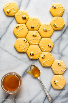 some cookies with bees on them next to a spoon and cup of honey dip sauce