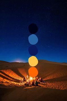 a group of people sitting around a campfire in the desert under a night sky