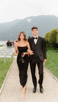 a man in a tuxedo and a woman in a black dress walking down a path