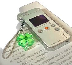 an old cell phone with a clover charm attached to it's side, sitting on top of a piece of paper