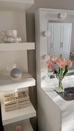 a vase filled with pink flowers sitting on top of a white shelf next to a mirror