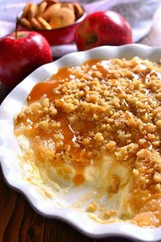 an apple crumbled dessert in a white dish on a wooden table next to apples