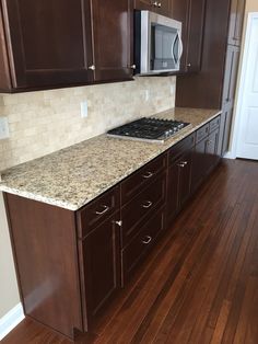 an empty kitchen with wooden floors and brown cupboards on one side, granite counter tops on the other