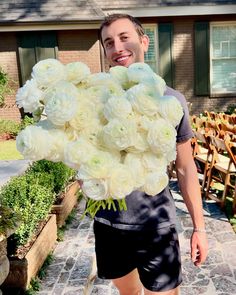 a man holding a large bouquet of white flowers in front of a house on a cobblestone walkway