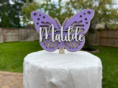 a purple butterfly cake topper sitting on top of a white table