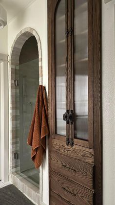 a towel hanging on the side of a wooden door next to a glass shower stall