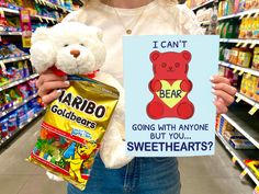 a person holding a sign and a teddy bear in a grocery store aisle with candy