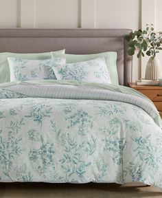 a bed with blue and white floral comforter set on it's headboard