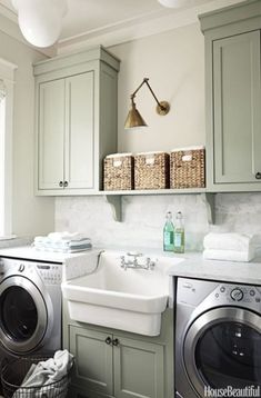 a washer and dryer in a small room with light green cabinets, white marble counter tops