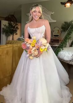 a woman in a white dress holding a bouquet of flowers and posing for the camera