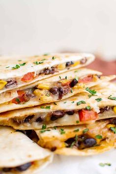 several tortillas stacked on top of each other with black beans, cheese and tomatoes