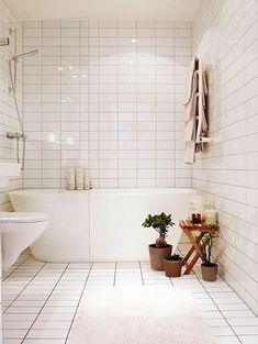 a white tiled bathroom with plants on the floor