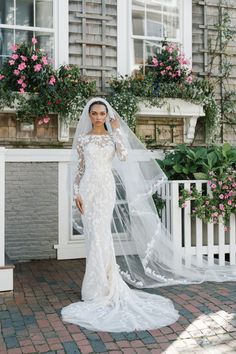 a woman in a wedding dress and veil standing on a brick walkway with pink flowers