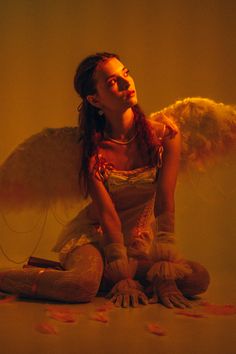 a woman sitting on the floor with an angel wings above her head and hair blowing in the wind