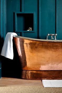 a wooden bathtub sitting on top of a floor next to a white towel and blue walls