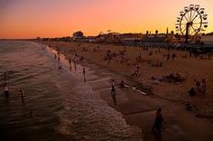 many people are on the beach and in the water at sunset or sunrise, with a ferris wheel in the background