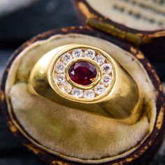 a gold ring with a red stone surrounded by small diamonds in it's case