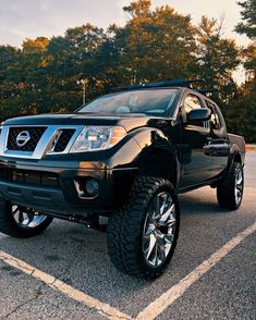 a black nissan truck parked in a parking lot next to trees and bushes on a sunny day