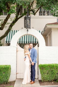 a man and woman standing in front of a white building with green striped awnings