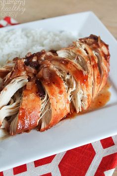 a white plate topped with meat covered in sauce next to rice on top of a red and white table cloth