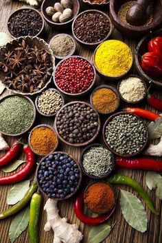 many different types of spices are arranged in bowls on a wooden table with leaves and peppers