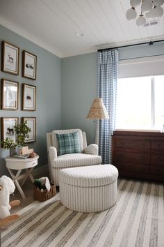 a baby's room with blue walls and striped rugs on the floor, white rocking chair in foreground