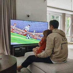 a man and child sitting in front of a tv watching soccer on the television screen