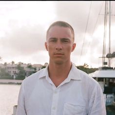 a man standing in front of a body of water with a boat in the background