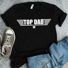 a t - shirt with the words top dad written in white on it next to jeans and sneakers