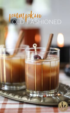 two glasses filled with liquid sitting on top of a metal tray next to an orange and white checkered table cloth