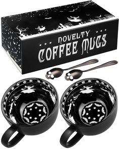 two black coffee mugs with spoons in front of a boxed box for novelty coffee mugs