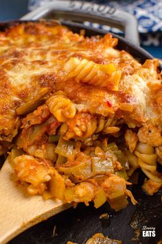 a skillet filled with pasta and vegetables on top of a wooden spatula next to an oven mitt