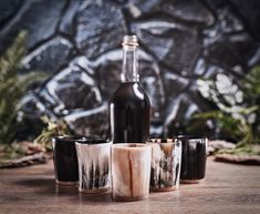 four shot glasses sitting on top of a wooden table next to a bottle of wine