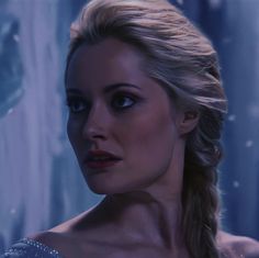 a woman with braids and blue eyes looks into the distance while standing in front of an icy background