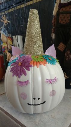 a white pumpkin decorated like a unicorn with flowers on its nose and eyelashes painted on it