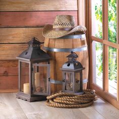 a wooden barrel with two lanterns and a straw hat on top sitting next to a window