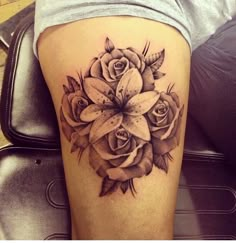 a black and white photo of a rose tattoo on the thigh, with lilies