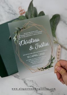 a person holding up a wedding card with greenery on it