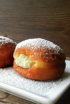 three doughnuts on a white plate with powdered sugar and cream filling them