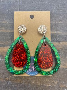 a pair of red and green glittered tear shaped earrings on top of a cardboard box