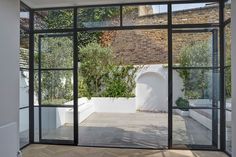 an open room with glass walls and potted plants on the wall, in front of a brick building