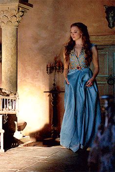 a woman in a blue dress standing next to a fireplace