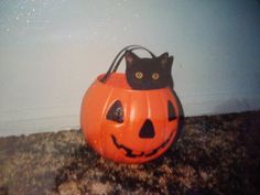 a black cat sitting inside of a pumpkin shaped basket on the ground with its eyes open