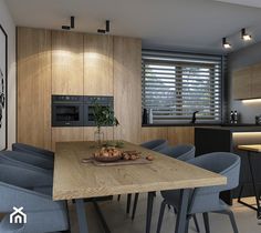 a dining room table with blue chairs in front of it and a kitchen behind it