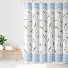 a shower curtain with birds on it in a white and light blue bathroom, next to a potted plant