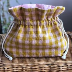 a yellow and pink checkered bag sitting on top of a wicker basket next to a potted plant