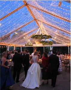 a group of people standing under a tent with lights on the ceiling and tables in front of them