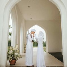 two people dressed in white are standing under an archway and touching their hands together while the man is wearing a turban